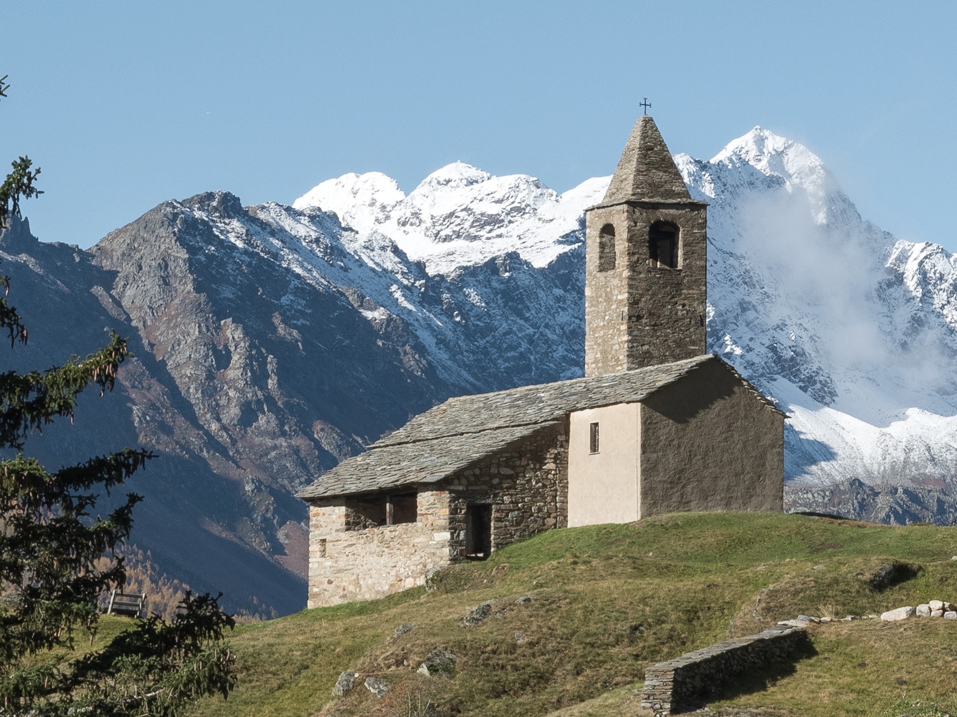 La chiesa romanica di San Romerio su un’altura, con sullo sfondo le montagne innevate della Valposchiavo