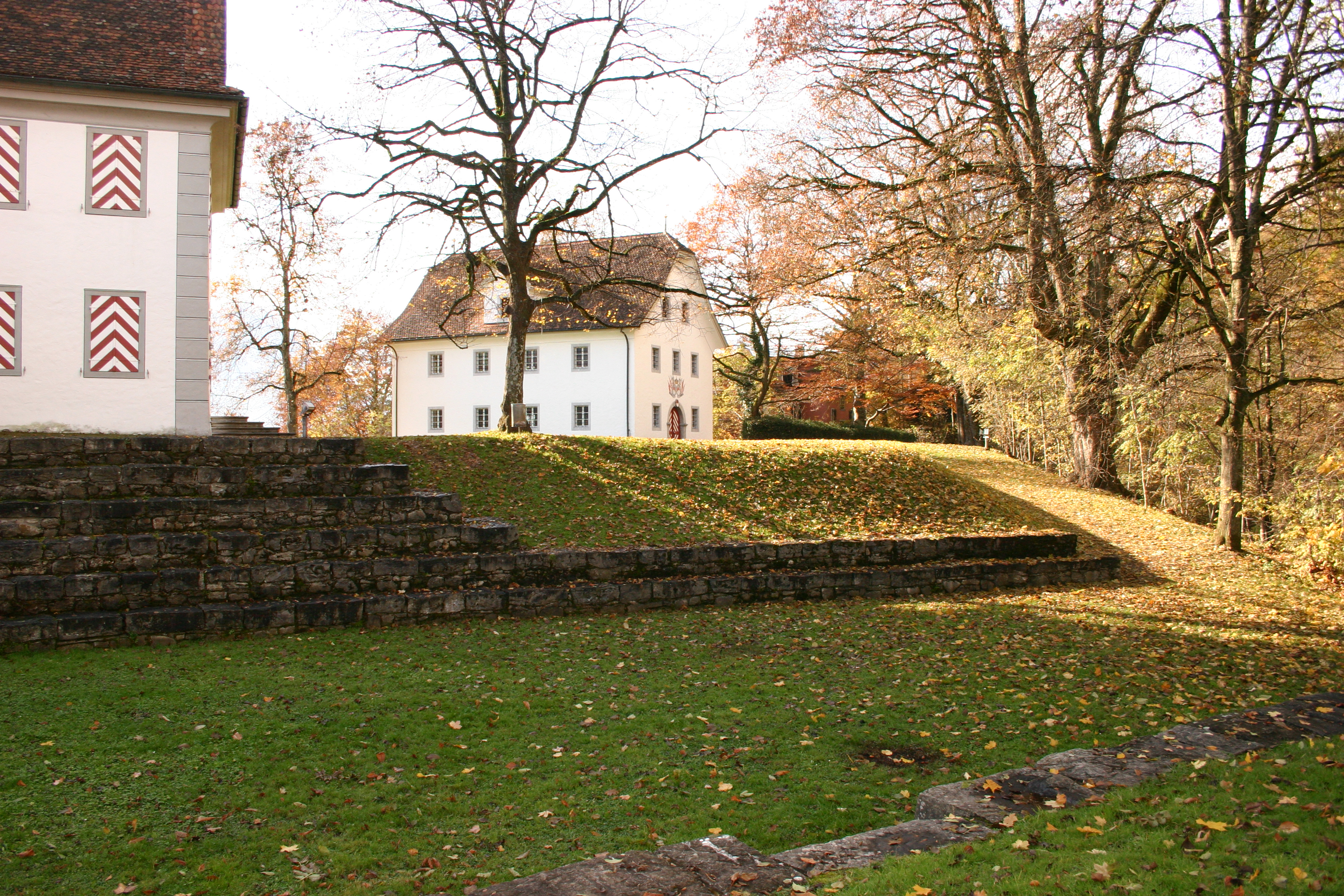 Auf dem Bild ist ein Teil der Burg Landenberg aus Sarnen zu sehen. Davor liegt eine Grüne Wiese mit jedoch kahlen Bäumen aus einem kühlen Herbsttag.